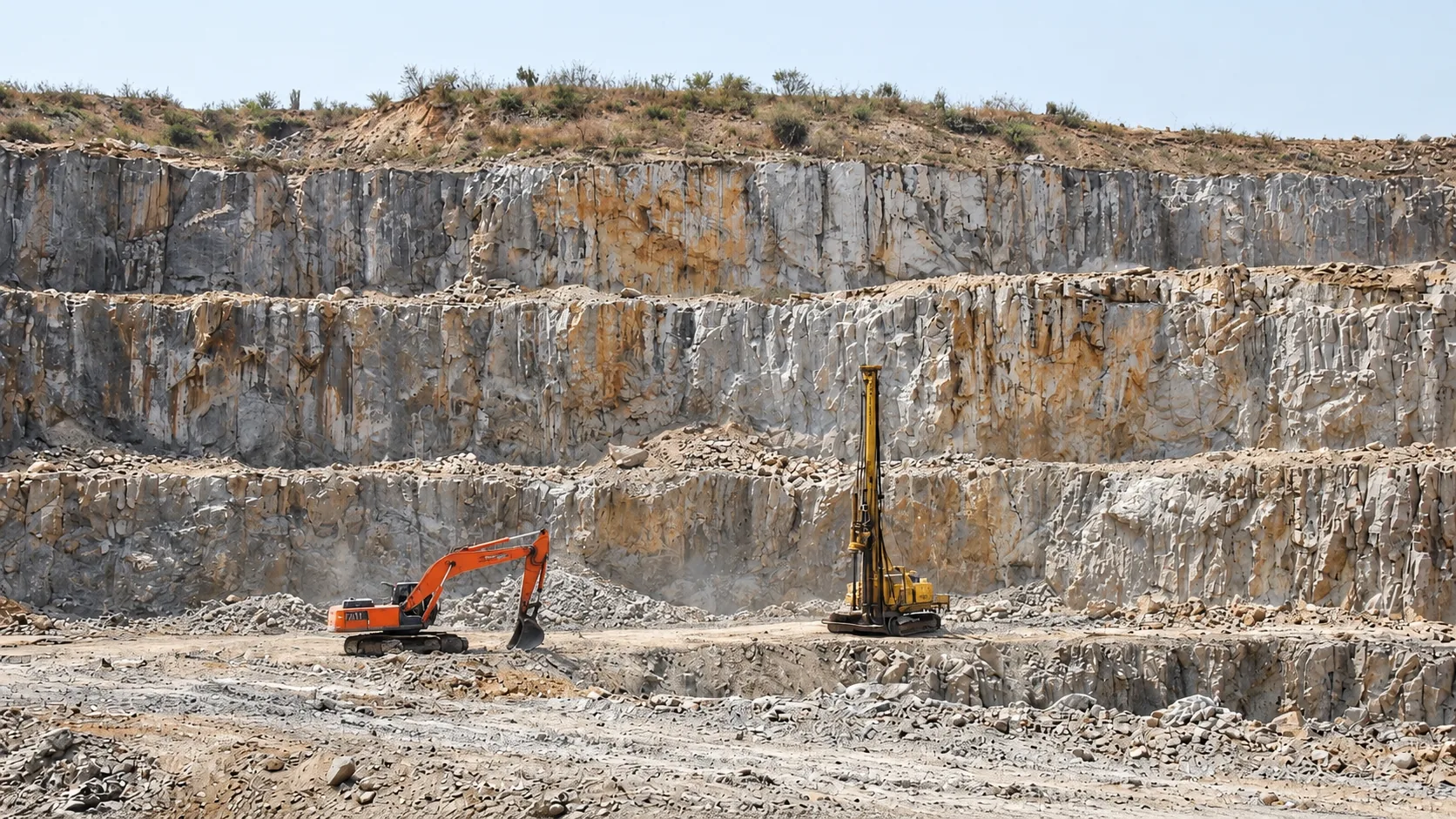 Benched quarry face with an excavator and a drill rig at its base