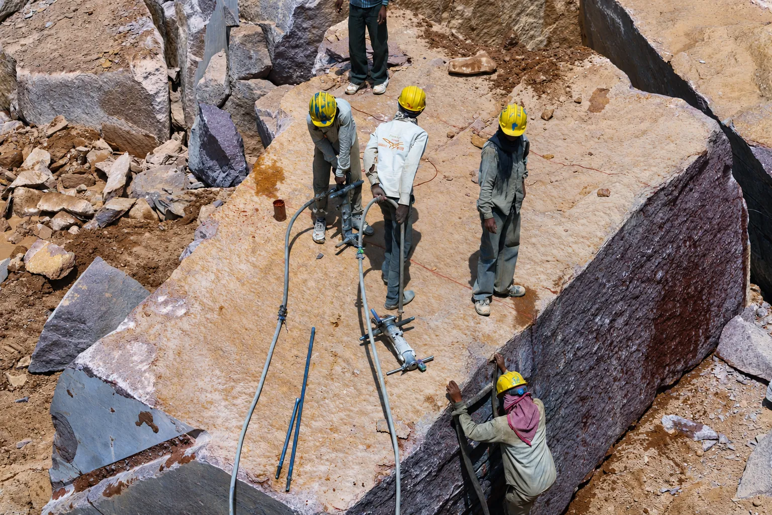 Top-down view of workers in yellow helmets drilling a granite block