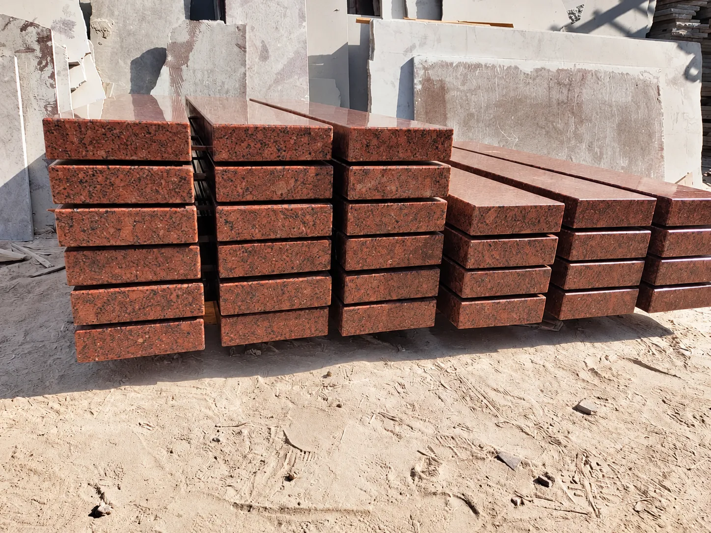 Polished red granite slabs and steps stacked on sand in a stone yard